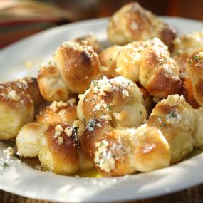 MINI GARLIC KNOTS - Our pizza dough rolled and tied into knots, baked, then smothered in melted butter and fresh garlic. Served with a side of marinara.