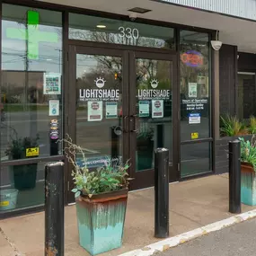 Close-up of the dispensary entrance with glass doors, signage, and potted plants.