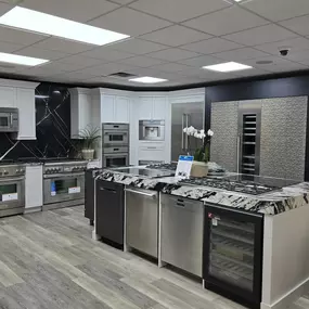 Clean, minimalistic kitchen design showcasing Bosch appliances, including a built-in wall oven, microwave, induction cooktop, and sleek dishwasher. The display features light wood cabinetry and a crisp white backsplash for a fresh look.