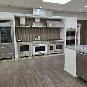 A luxury kitchen appliance display featuring a Sub-Zero built-in refrigerator with custom cabinetry panels, paired with Wolf’s professional-grade red-knob range and built-in wall oven, displayed in a premium designer kitchen setup.