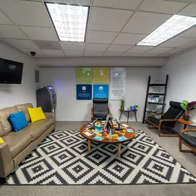 The lounge area at Lightshade Evans Dispensary, featuring a cozy setup with a patterned rug, leather couch, coffee table, and informational posters on the wall.