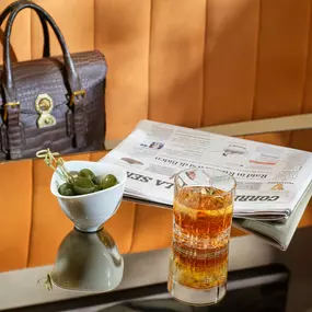 One of the tables in Il Salotto Lobby Lounge with a cocktail, green olives and a newspaper.