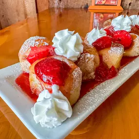 Cinnamon Sugar Balls Topped with Strawberry Glaze, Whipped Cream, and powdered Sugar.