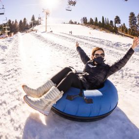 Hands raised high as you glide down on a winter snow tube.