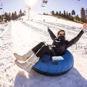 Hands raised high as you glide down on a winter snow tube.