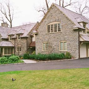 Interior and exterior renovations to this Bryn Mawr stone manor home. Photo shows new stone facade on garage, dentil moldings at roof line, new windows, copper roof portico, new pent roof over garage doors with corbels. Interior work includes a new kitchen, and a full basement remodel.