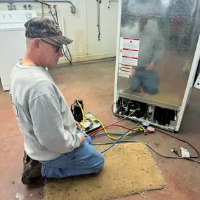 A technician kneeling to repair a refrigerator at Flick Brothers Electric.