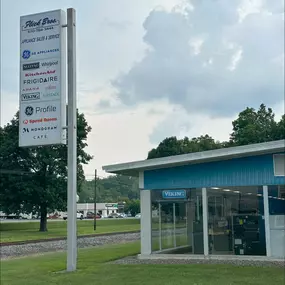 Tall Flick Brothers Electric sign listing brands, with the blue showroom in the background.