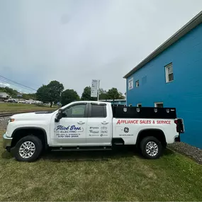 Flick Brothers Electric branded pickup truck parked next to the blue building.