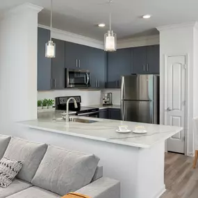 Gorgeous open kitchen with gray cabinetry, kitchen pantry, quartz countertops, undermount sink with gooseneck spray faucet, and pendant lighting