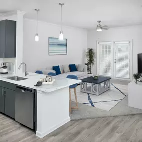 Open kitchen with stainless steel appliances, grey cabinetry, and quartz countertops.