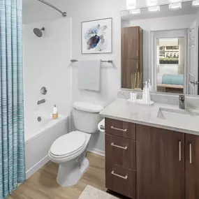 Camden San Marcos Apartments Scottsdale AZ bathroom with white quartz countertop, plenty of room for storage including a linen closet, and brushed nickel fixtures including a curved shower rod