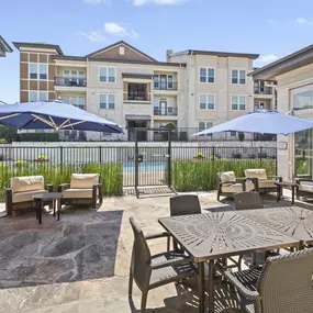 Patio deck lounge with large umbrella-covered seating by the pool at Camden La Frontera apartments in Round Rock, TX