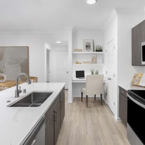 Kitchen with marble-style white quartz countertops, stainless steel appliances, modern brown cabinets, white subway tile backsplash, and built-in desk at Camden Panther Creek apartments in Frisco, TX