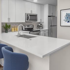 Modern kitchen with white quartz countertops, white cabinetry, and hardwood-style flooring.