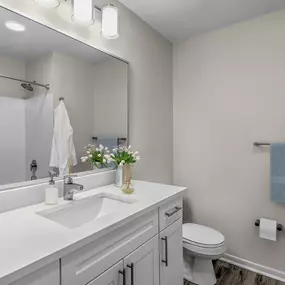 Modern bathroom with white quartz countertops, hardwood-style flooring, and bathtub and shower combination with tile surround