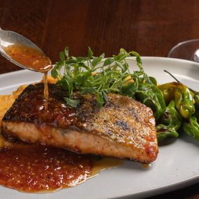 Crispy Skin Sweet Chili Salmon with the sauce being spooned on at The Independent in the Theatre District.