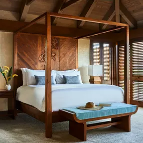 Bedroom with wooden canopy bed, ceiling fan, and open shutters.