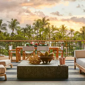 Outdoor lounge area at sunset with lawn and palm trees.