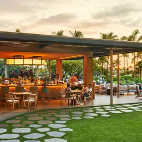 Outdoor bar and dining area at sunset with lawn and palm trees.