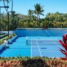 Tennis court bordered by palm trees and tropical landscaping.