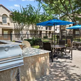 Poolside grills and umbrella-covered seating at Camden Cimarron apartments in Irving, TX