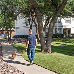 Resident walking a dog on a sidewalk in a courtyard at Camden Legacy Park