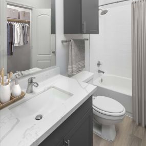Bathroom with marble-style countertops, gray cabinetry, bathtub and walk-in closet