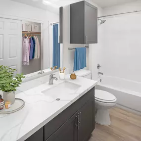 Bathroom with marble-style countertops, gray cabinetry, bathtub and walk-in closet