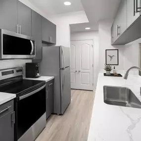 Newly renovated kitchen with marble-style quartz countertops, dark gray cabinets, and white subway tile backsplash at Camden Legacy Park apartments in Plano, TX