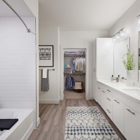 Contemporary Style bathroom with double sink, quartz countertops, hardwood-style flooring, bathtub shower combination, and walk-in closet.