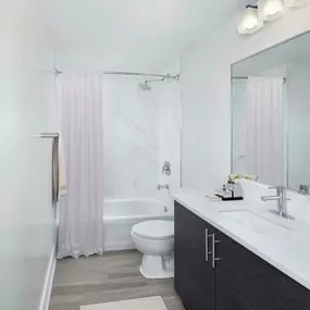 Bathroom with wood-inspired flooring and curved shower rod at Camden Brickell apartments in Miami, FL