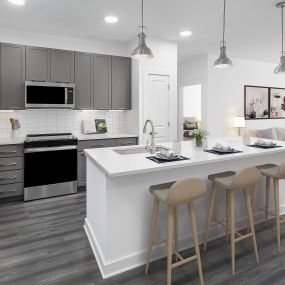 Camden Tempe West Apartments Tempe Arizona open concept contemporary kitchen with stainless steel appliances including a side-by-side refrigerator, white quartz countertops, designer pendant lighting and gray wood-like flooring