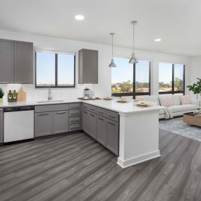 Camden Tempe West Apartments Tempe Arizona contemporary open concept windowed kitchen with white quartz countertops, stainless steel appliances, gray cabinetry, large pantry, and wood-like flooring throughout with floor to ceiling windows in nearby living room