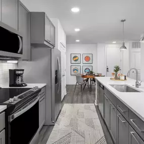 Camden Tempe West Apartments in Tempe Arizona luxury kitchen with stainless steel appliances white quartz countertop gray cabinetry and wood-like flooring, white subway tile backsplash and under cabinet lighting near dining area