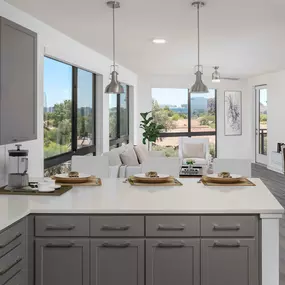 Camden Tempe West Apartments Tempe Arizona contemporary kitchen with modern gray shaker cabinets white quartz countertops and pendant lighting near open concept living room with ceiling fan and floor to ceiling windows