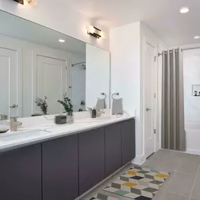 Bathroom with dual vanity, large mirror, gray tile flooring and bathtub shower combination with tile surround