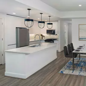 White contemporary kitchen and dining room with hardwood-style flooring, pendant lighting, and white quartz countertops and whit