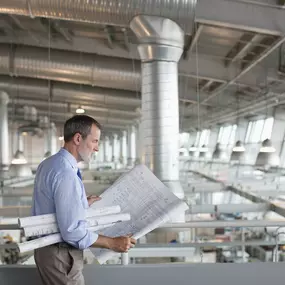 A professional architect reviews blueprints inside a modern industrial facility, emphasizing precision, design expertise, and attention to detail in large-scale commercial construction and engineering projects.