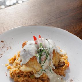 A piece of fish served on a bed of rice and topped with a cream sauce
