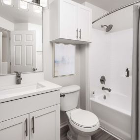 Bathroom with white shaker cabinets, white quartz countertops, brushed nickel fixtures and curved shower rod