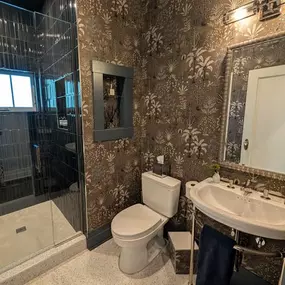 This bathroom is a showstopper complete with gorgeous tile work, a gleaming glass shower, and rich, textured wallpaper.  High ceilings and eye-catching light fixtures complete the elegant feel.