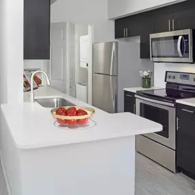 Modern kitchen with white quartz countertops, large breakfast bar, soft close cabinets, and stainless steel appliances at Camden Lee Vista apartments in Orlando, FL