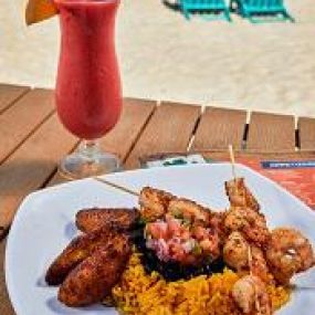 grilled shrimp skewers on a bed of rice with black beans and plantains with frozen margarita on the side.