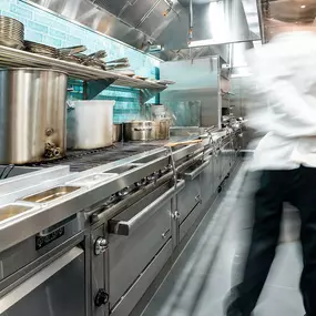 A professional chef moves through a stainless steel commercial kitchen, showcasing Singer Equipment’s restaurant design expertise