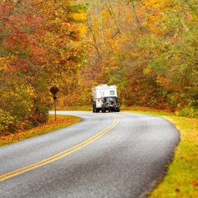 A photo of an RV with a trailer hitch flat towing a jeep in the fall.