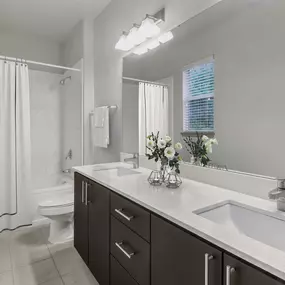 Bathroom with double sinks, cabinet storage, a window with natural light, and a shower/bathtub at Camden Asbury Village in Raleigh, NC.