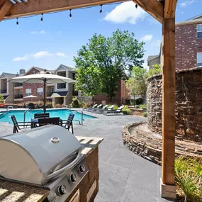 Covered grilling area near pool with water feature and dining table