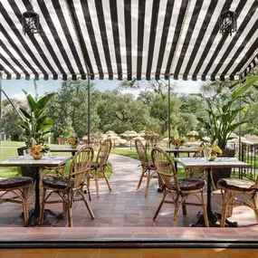 Covered patio with striped pergola and dining tables overlooking greenery.