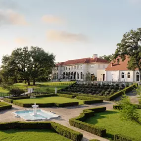 Expansive garden lawn with fountains and a stately building in the background.